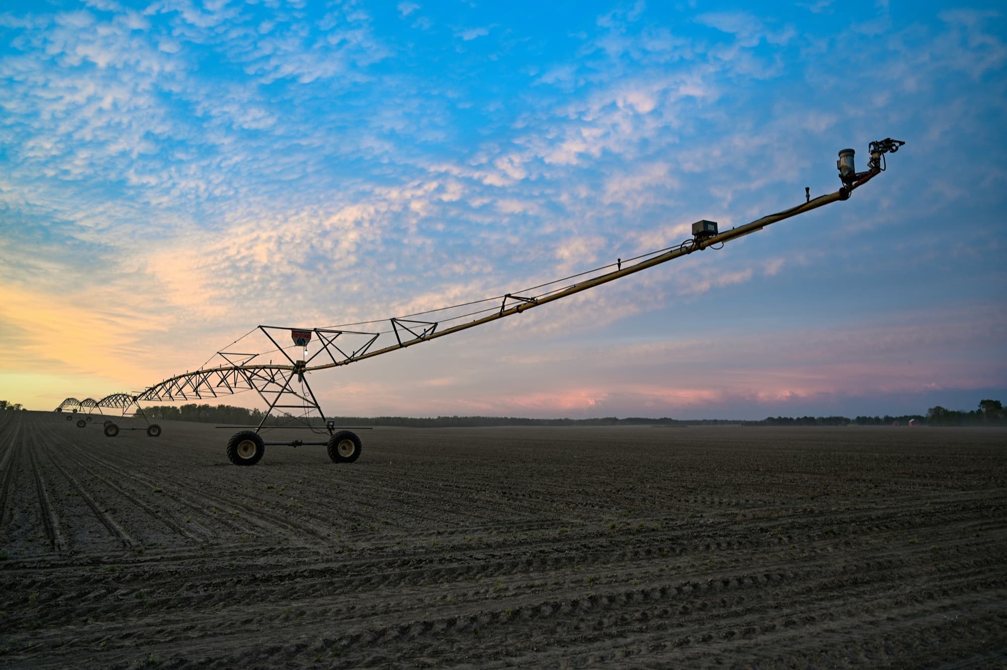 A centre-pivot irrigation boom over a freshly planted field at sunset