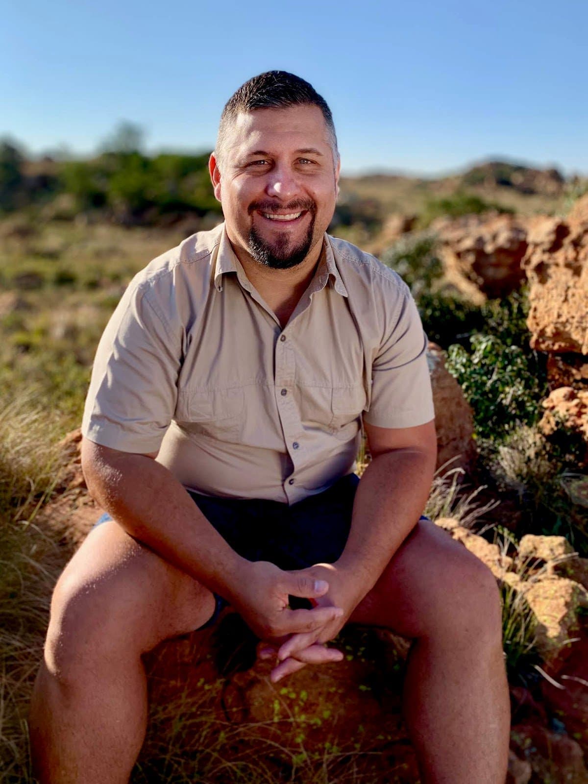 Farmer smiling, sitting on rocks in the veld on a sunny day